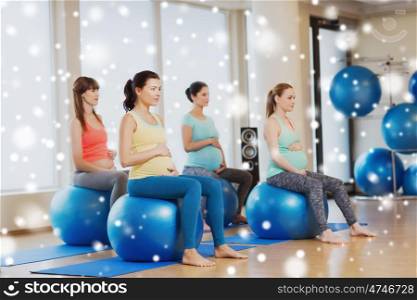 pregnancy, sport, fitness, people and healthy lifestyle concept - group of happy pregnant women exercising on stability balls in gym over snow