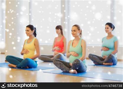 pregnancy, sport, fitness, people and healthy lifestyle concept - group of happy pregnant women exercising yoga in lotus pose in gym over snow. happy pregnant women exercising yoga in gym
