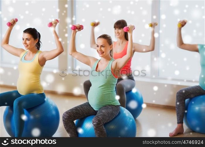 pregnancy, sport, fitness, people and healthy lifestyle concept - group of happy pregnant women with dumbbells exercising on stability balls in gym over snow
