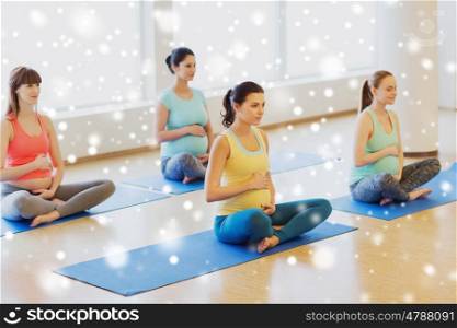 pregnancy, sport, fitness, people and healthy lifestyle concept - group of happy pregnant women exercising yoga in lotus pose in gym over snow
