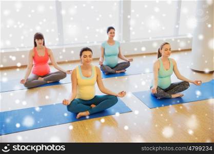 pregnancy, sport, fitness, people and healthy lifestyle concept - group of happy pregnant women exercising yoga and meditating in lotus pose in gym over snow