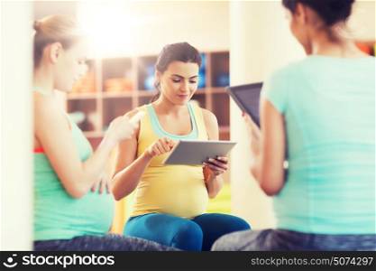 pregnancy, sport, fitness, people and healthy lifestyle concept - group of happy pregnant women with tablet pc computer and smartphone sitting on balls in gym. happy pregnant women with gadgets in gym