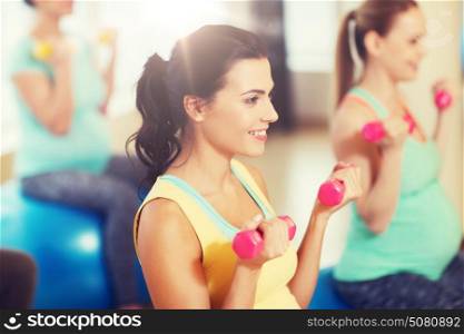 pregnancy, sport, fitness, people and healthy lifestyle concept - group of happy pregnant women with dumbbells exercising on ball in gym. happy pregnant women exercising on fitball in gym