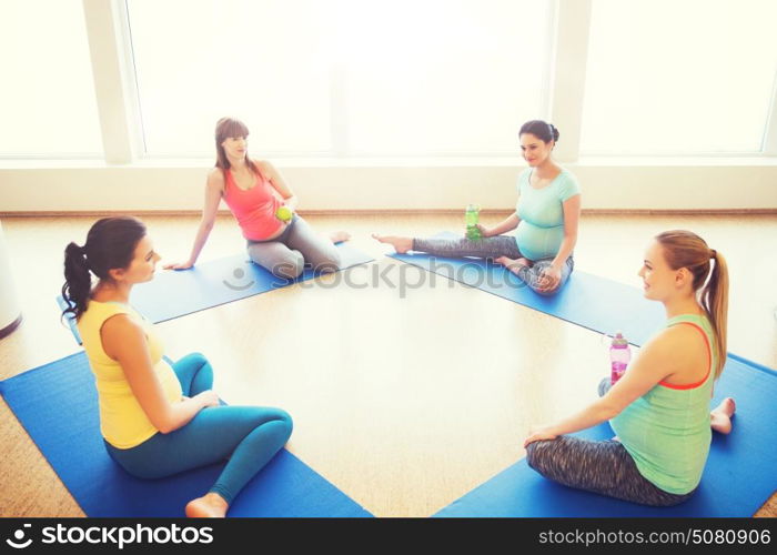 pregnancy, sport, fitness, people and healthy lifestyle concept - group of happy pregnant women with water bottles sitting on mats and talking in gym. happy pregnant women sitting on mats in gym