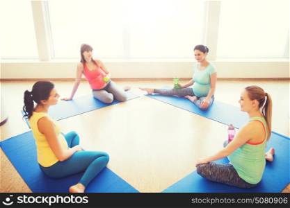 pregnancy, sport, fitness, people and healthy lifestyle concept - group of happy pregnant women with water bottles sitting on mats and talking in gym. happy pregnant women sitting on mats in gym