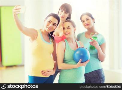 pregnancy, sport, fitness, people and healthy lifestyle concept - group of happy pregnant women with sports stuff taking selfie by smartphone in gym. pregnant women taking selfie by smartphone in gym. pregnant women taking selfie by smartphone in gym