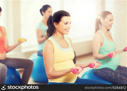 pregnancy, sport, fitness, people and healthy lifestyle concept - group of happy pregnant women with dumbbells exercising on ball in gym. happy pregnant women exercising on fitball in gym. happy pregnant women exercising on fitball in gym