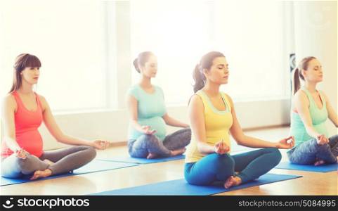 pregnancy, sport, fitness, people and healthy lifestyle concept - group of happy pregnant women exercising yoga and meditating in lotus pose in gym. happy pregnant women exercising yoga in gym. happy pregnant women exercising yoga in gym