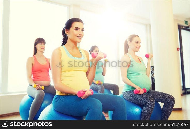 pregnancy, sport, fitness, people and healthy lifestyle concept - group of happy pregnant women with dumbbells exercising on ball in gym. happy pregnant women exercising on fitball in gym