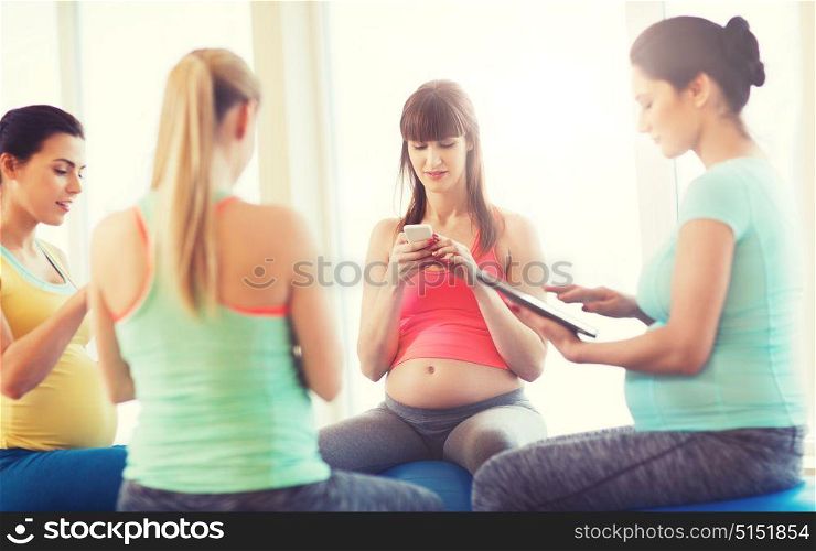 pregnancy, sport, fitness, people and healthy lifestyle concept - group of happy pregnant women with tablet pc computer and smartphone sitting on balls in gym. happy pregnant women with gadgets in gym