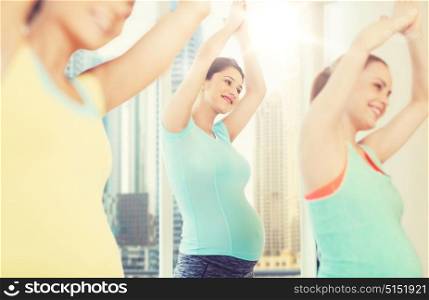pregnancy, sport, fitness, people and healthy lifestyle concept - group of happy pregnant women exercising in gym over city window view background. happy pregnant women exercising in gym
