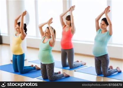 pregnancy, sport, fitness, people and healthy lifestyle concept - group of happy pregnant women exercising on mats in gym