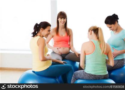pregnancy, sport, fitness, people and healthy lifestyle concept - group of happy pregnant women sitting and talking on balls in gym