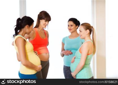 pregnancy, sport, fitness, people and healthy lifestyle concept - group of happy pregnant women talking in gym