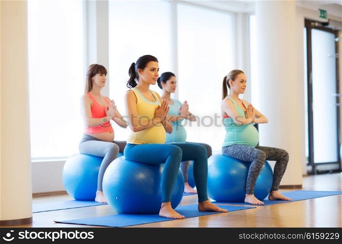 pregnancy, sport, fitness, people and healthy lifestyle concept - group of happy pregnant women exercising on ball in gym