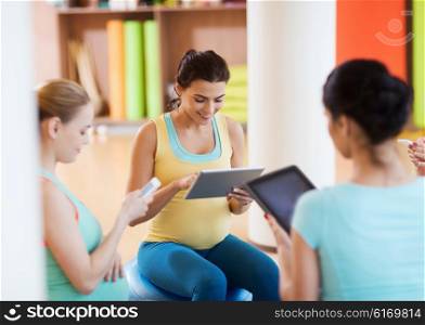 pregnancy, sport, fitness, people and healthy lifestyle concept - group of happy pregnant women with tablet pc computer and smartphone sitting on balls in gym