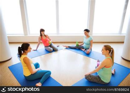 pregnancy, sport, fitness, people and healthy lifestyle concept - group of happy pregnant women with water bottles sitting on mats and talking in gym