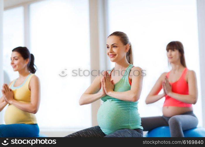 pregnancy, sport, fitness, people and healthy lifestyle concept - group of happy pregnant women exercising on ball in gym