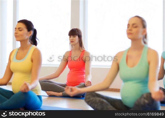 pregnancy, sport, fitness, people and healthy lifestyle concept - group of happy pregnant women exercising yoga and meditating in lotus pose in gym