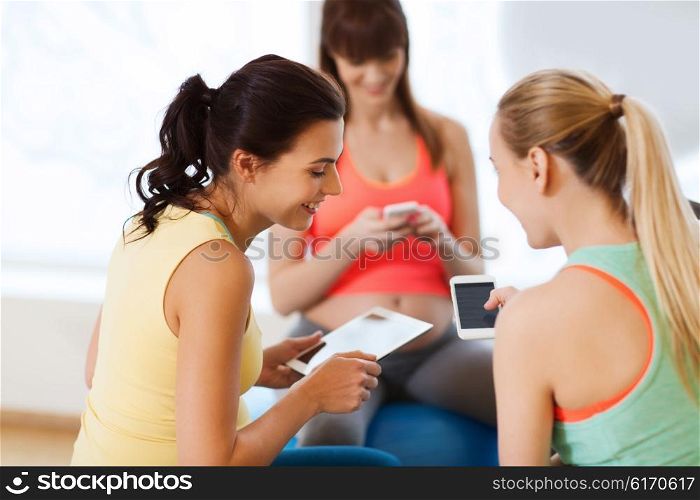 pregnancy, sport, fitness, people and healthy lifestyle concept - group of happy pregnant women with tablet pc computer and smartphone sitting on balls in gym
