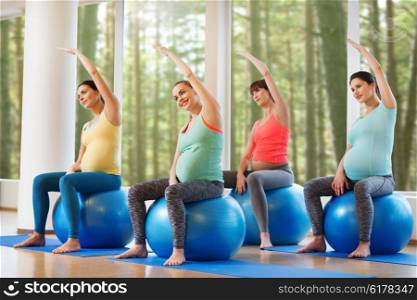 pregnancy, sport, fitness, people and healthy lifestyle concept - group of happy pregnant women exercising on ball in gym