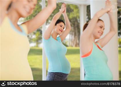 pregnancy, sport, fitness, people and healthy lifestyle concept - group of happy pregnant women exercising in gym over natural window view background
