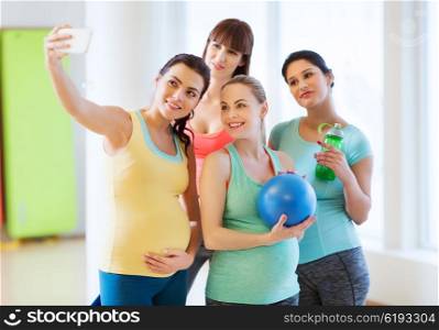 pregnancy, sport, fitness, people and healthy lifestyle concept - group of happy pregnant women with sports stuff taking selfie by smartphone in gym