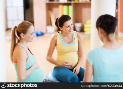pregnancy, sport, fitness, people and healthy lifestyle concept - group of happy pregnant women sitting and talking on balls in gym