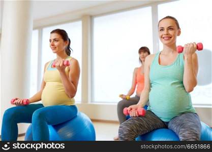 pregnancy, sport, fitness, people and healthy lifestyle concept - group of happy pregnant women with dumbbells on exercise ball in gym. pregnant women training with exercise balls in gym