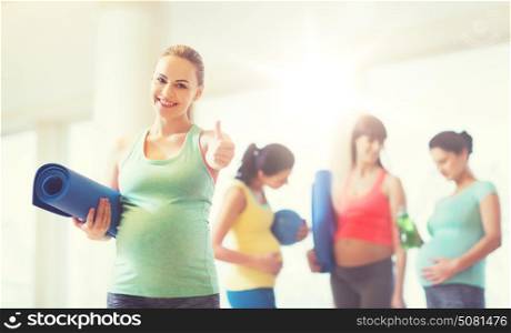 pregnancy, sport, fitness, people and healthy lifestyle concept - happy pregnant woman with mat in gym showing thumbs up . pregnant woman with mat in gym showing thumbs up