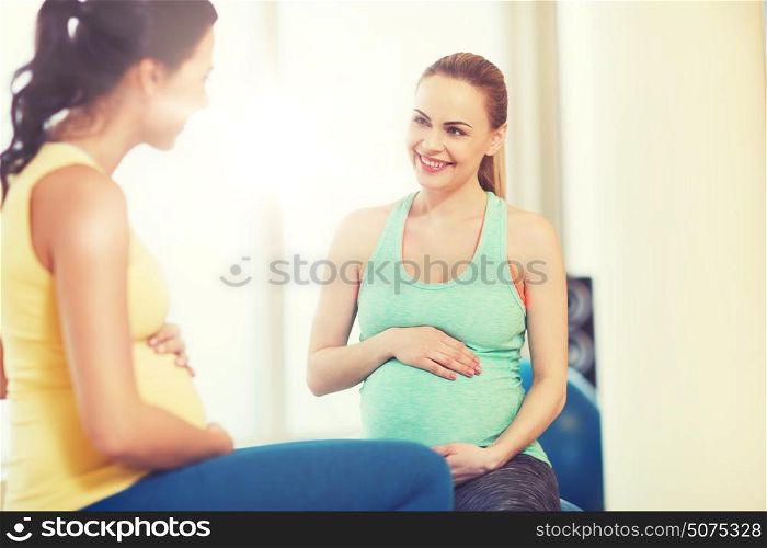 pregnancy, sport, fitness, people and healthy lifestyle concept - two happy pregnant women sitting and talking on balls in gym. two happy pregnant women sitting on balls in gym