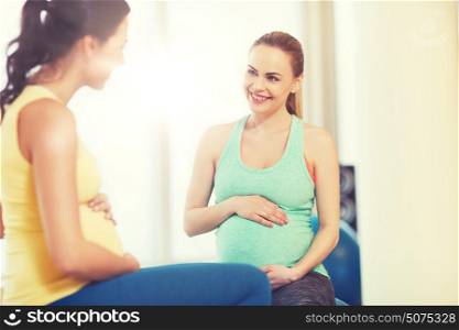 pregnancy, sport, fitness, people and healthy lifestyle concept - two happy pregnant women sitting and talking on balls in gym. two happy pregnant women sitting on balls in gym