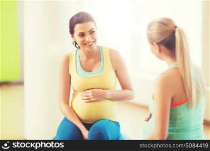 pregnancy, sport, fitness, people and healthy lifestyle concept - two happy pregnant women sitting and talking on balls in gym. two happy pregnant women sitting on balls in gym. two happy pregnant women sitting on balls in gym
