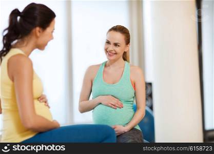 pregnancy, sport, fitness, people and healthy lifestyle concept - two happy pregnant women sitting and talking on balls in gym