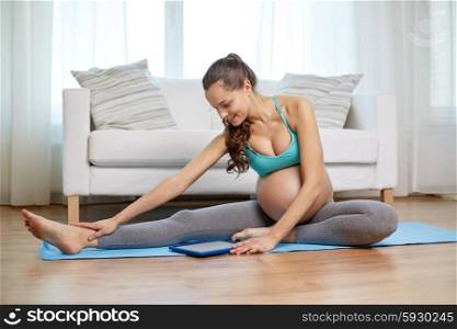 pregnancy, sport, people and technology concept - happy pregnant woman with tablet pc computer exercising and stretching leg on mat at home
