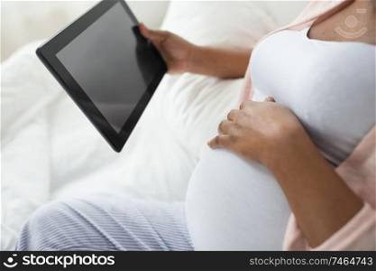 pregnancy, technology and people concept - close up of pregnant african american woman with tablet pc computer in bed at home. close up of pregnant woman with tablet pc at home