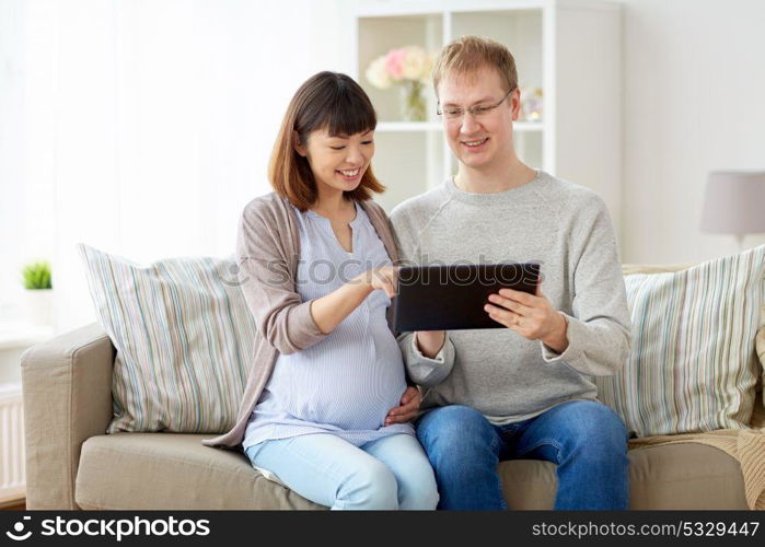pregnancy, technology and people concept - happy husband and his pregnant wife with tablet pc computer at home. husband and pregnant wife with tablet pc at home
