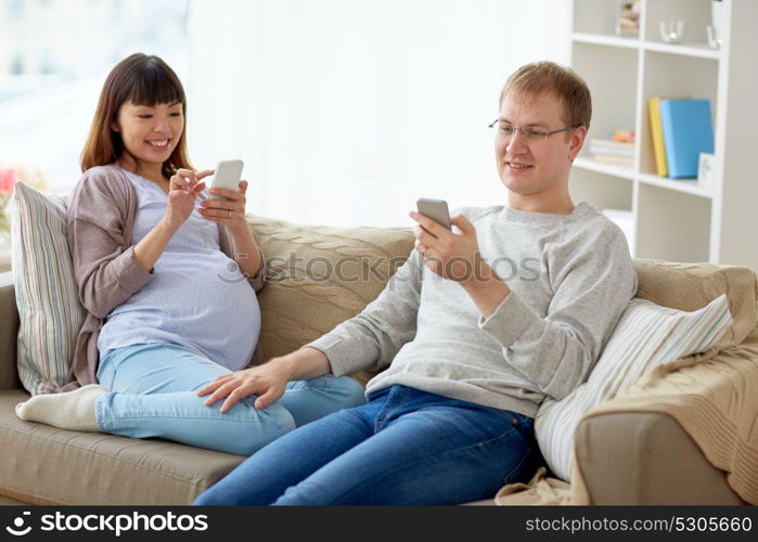 pregnancy, technology and people concept - happy husband and his pregnant wife with smartphones at home. husband and pregnant wife with smartphone at home