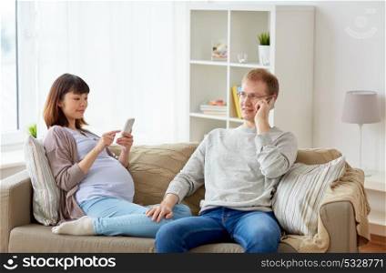 pregnancy, technology and people concept - happy husband and his pregnant wife with smartphones at home. husband and pregnant wife with smartphone at home