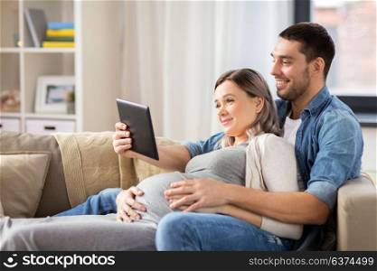 pregnancy, technology and people concept - happy man and his pregnant wife with tablet pc computer at home. man and pregnant woman with tablet pc at home
