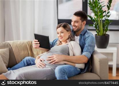 pregnancy, technology and people concept - happy man and his pregnant wife with tablet pc computer at home. man and pregnant woman with tablet pc at home. man and pregnant woman with tablet pc at home
