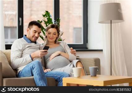 pregnancy, technology and people concept - happy man and his pregnant wife with smartphones at home. man and pregnant wife with smartphone at home