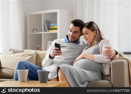 pregnancy, technology and people concept - happy man and his pregnant wife with smartphones at home. man and pregnant wife with smartphone at home. man and pregnant wife with smartphone at home