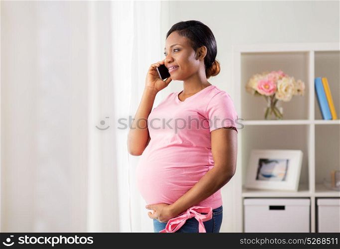 pregnancy, technology and people concept - happy pregnant african american woman calling on smartphone and looking through window at home. happy pregnant woman calling on smartphone at home