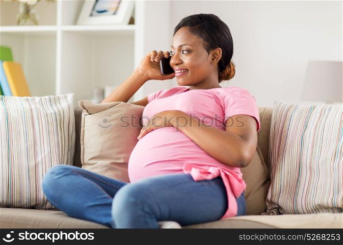 pregnancy, technology and people concept - happy pregnant african american woman calling on smartphone at home. happy pregnant woman calling on smartphone at home