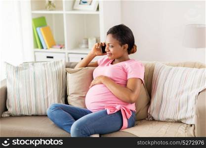 pregnancy, technology and people concept - happy pregnant african american woman calling on smartphone at home. happy pregnant woman calling on smartphone at home