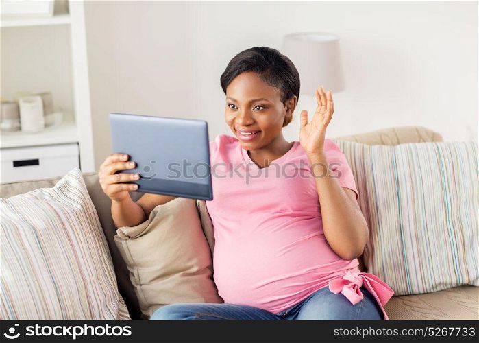 pregnancy, technology and people concept - happy pregnant african american woman with tablet pc computer having video call and waving hand at home. happy pregnant woman with tablet pc at home
