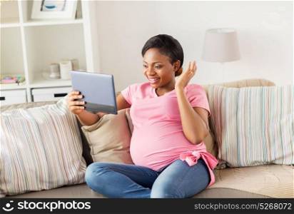 pregnancy, technology and people concept - happy pregnant african american woman with tablet pc computer having video call and waving hand at home. happy pregnant woman with tablet pc at home