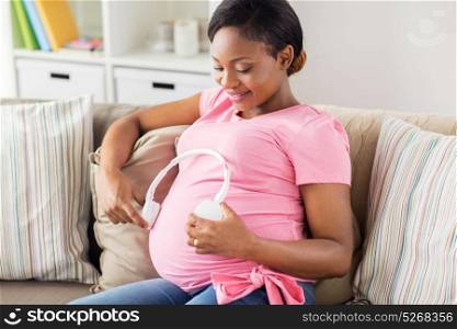 pregnancy, technology and people concept - happy pregnant african american woman with headphones on her belly at home. pregnant woman with headphones at home