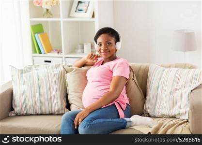 pregnancy, technology and people concept - happy pregnant african american woman with headphones listening to music at home. pregnant woman in headphones at home